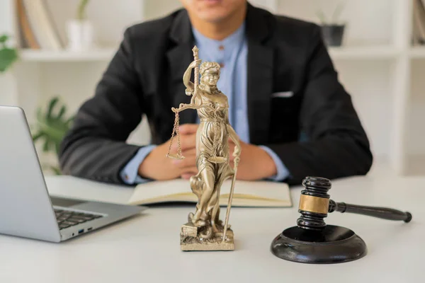 the goddess of justice with scales and hammers placed in front of a Male lawyer working on a laptop legal concept. Advice on Justice in the Lawyer\'s Office