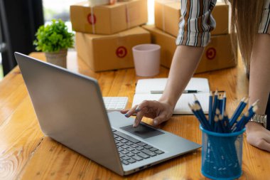 Çevrimiçi satış ve paketleme kavramları ve çevrimiçi pazarlama dağıtımı olan bir dizüstü bilgisayar üzerinde çalışan küçük bir işletme KOBİ girişimcisi veya bağımsız genç Asyalı kadın başlatın. KME kavramları.