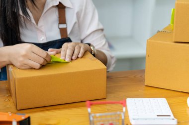 Çevrimiçi satış ve paketleme kavramları ve çevrimiçi pazarlama dağıtımı olan bir dizüstü bilgisayar üzerinde çalışan küçük bir işletme KOBİ girişimcisi veya bağımsız genç Asyalı kadın başlatın. KME kavramları.