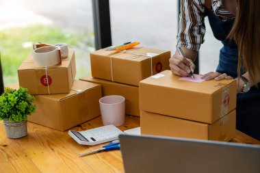 Çevrimiçi satış ve paketleme kavramları ve çevrimiçi pazarlama dağıtımı olan bir dizüstü bilgisayar üzerinde çalışan küçük bir işletme KOBİ girişimcisi veya bağımsız genç Asyalı kadın başlatın. KME kavramları.