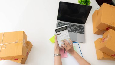 Çevrimiçi satış ve paketleme kavramları ve çevrimiçi pazarlama dağıtımı olan bir dizüstü bilgisayar üzerinde çalışan küçük bir işletme KOBİ girişimcisi veya bağımsız genç Asyalı kadın başlatın. KME kavramları.