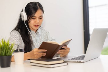 Genç öğrenciler çevrimiçi çalışmak için bilgisayar kullanır. Çevrimiçi eğitim ve Asyalı kadın öğrenimi masasında oturup yaratıcı işler yaparken dizüstü bilgisayar teknolojisi kullanıyor. ev kavramından çalışma