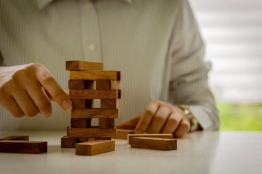 Kadının eli ahşap bloğu çekti. İş başarısı kavramları, planlama, risk ve iş stratejisi. İş adamı kulede tahta bir blok tutuyor.