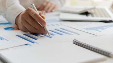 Finansal istatistik veri analiz çizelgeleri, grafikleri ve hesap makineleri olan bir iş kadını elinde tutuyor. Finansal konsept elinde kalem tutarak finansal bir belgeyi işaret ediyor