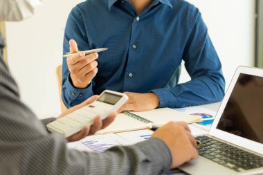 İşletme ekibi dosyaları, kalemleri ve analitik kağıtları ofis masasında tutarak projeleri tartışıyor ve planlıyor. Arka planda dizüstü bilgisayarı ve finansal grafiği var. iş fikri