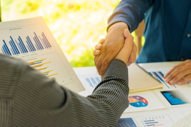 Modern ofis işbirliği anlaşması ve masadaki mali kağıt grafiğini yaptıktan sonra işadamları ofis penceresinin yanında dururken el sıkışıyor
