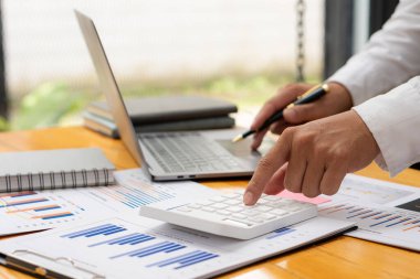 Bir muhasebeci hesap makinesine, aylık finansal rapor ya da şirket karını çizelge kağıtları ve evden ideal bir dizüstü bilgisayarla masasında yapmak için baskı yapar..