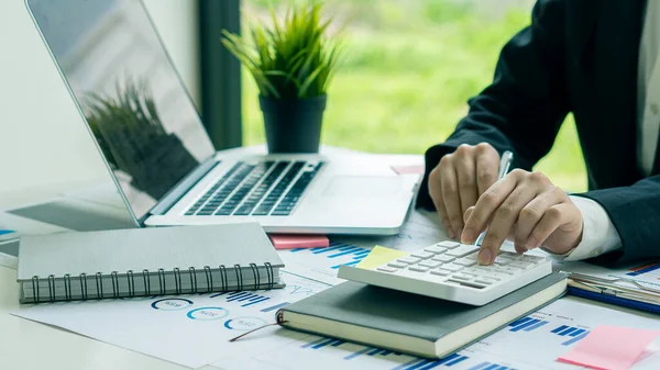 会計士は計算機を押して毎月の財務報告書や会社の利益を彼の机の上にグラフ用紙と理想的なラップトップで作る — ストック写真