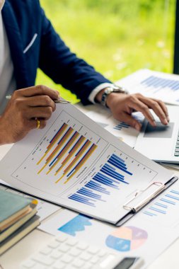 Elinde kalem tutan işadamı masadaki kağıt finans grafiğini incelemeye ve hesap makinesiyle çalışan işletmeler ve muhasebeciler için yatırım planına işaret ediyor..