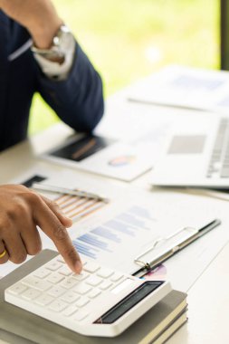 Elinde kalem tutan işadamı masadaki kağıt finans grafiğini incelemeye ve hesap makinesiyle çalışan işletmeler ve muhasebeciler için yatırım planına işaret ediyor..