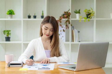 Modern bir ofiste tablet bilgisayarlar ve finansal grafikler üzerinde çalışan serbest çalışan Asyalı bir kadın. bir hesap analizi raporu hazırlamak gayrimenkul yatırım bilgileri finans ve vergi sistemi kavramları