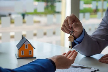 Satış temsilcisi bir ev veya daire satın almak için sözleşme sunar ve müşteriye bir ev anahtarı zinciri verir ve emlak satın almak veya satmak için kredi ve faiz oranı fikirlerini tartışır.
