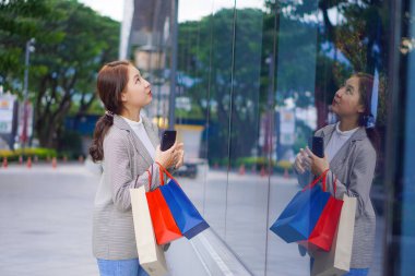 Bir butiğin önünde elinde bir alışveriş çantası olan güzel bir kız. Satış sezonunda alışveriş yaparken alışveriş yapmaktan hoşlanan zarif bir genç kadının portresi.