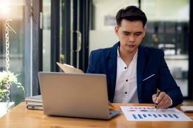 Genç Asyalı işadamı sunumlar için masanın üstünde veri grafiği ve hesap makinesi laptopu üzerinde çalışıyor. Profesyonel iş adamları iş bilgileri finansal belgelerle meşguller.