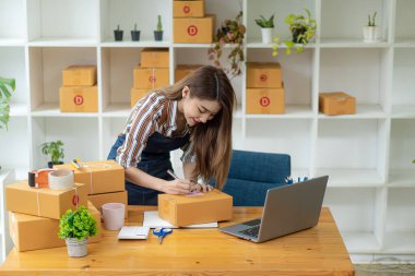 Küçük işletme, KME girişimi, kutularla çalışan Asyalı kadın girişimcilerin sahibi ve ürün kutularını hazırlamak için akıllı telefon veya dizüstü bilgisayar kullanımı ve çevrimiçi siparişleri kontrol etmek. İnternetten satış fikirleri sat..