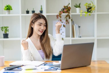 Ofisteki pazarlama finans verilerini analiz eden grafikler ve dizüstü bilgisayarlarla çalışan genç Asyalı iş kadını.