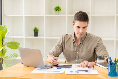 İşadamı, bilgisayar, dizüstü bilgisayar ve belgelerle ön görüş alanındaki grafikleri analiz ederek çalışır. Ahşap bir masada otururken ofiste çalışan finansal piyasa analisti.