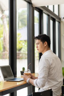 Genç Asyalı bir adam, kaplan derisi ve bir fincan kahveyle bir kafede çalışmayı öğrenmenin yanında dizüstü bilgisayarda çalışıyor..