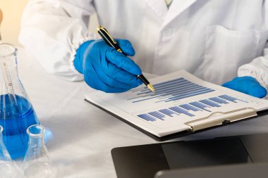 Doktor yanında dizüstü bilgisayarı olan bir kalem ve test şişesi tutuyor..