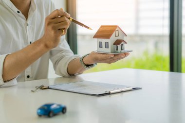 The sales representative holds a model house in the office. Real Estate Buying or Selling Ideas The sales representative offers a home purchase contract to purchase the house and car on the table.