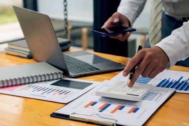 Businessman working with smartphone and graph with the laptop to analyze financial data and calculator to calculate earnings.