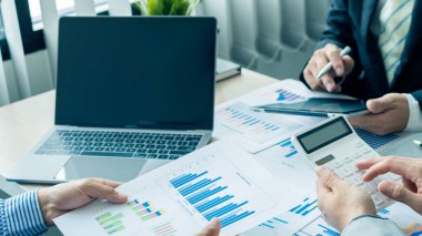 Businessman Discussing Successful Teamwork Teamwork Charts and Graphs Businessman working in the office discussing papers and ideas in meeting with laptop and calculator to calculate and analyze.