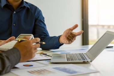 Businessman Discussing Successful Teamwork Teamwork Charts and Graphs Businessman working in the office discussing papers and ideas in meeting with laptop and calculator to calculate and analyze.