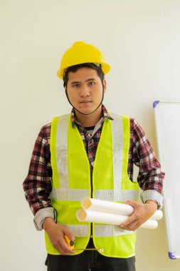Genç bir mühendis elinde bir kağıt yazıcı ve sarı kasklı bir mezura tutuyor..