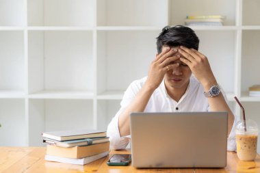 Genç bir adam iş yerinde dizüstü bilgisayar, kaplan derisi kahve fincanı ve akıllı telefonuyla oturuyor..