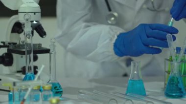 Maskeli erkek bilim adamı, ilaç biyoteknoloji gelişimi için gelişmiş bilimsel laboratuvarı analiz etmek için mikro pipet kullanıyor. Tıbbi araştırmalar yapan bilim adamları tüp bebek deneyleri yapıyor..