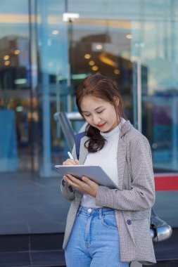 Bir alışveriş merkezinin önünde elinde çantası olan Asyalı bir kadın dışarıda çalışma fikirleri satıyor..