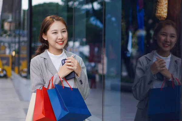 一位快乐 面带微笑的亚洲少女站在购物中心前 手里拿着一个五颜六色的购物袋和一部手机 生活方式技术概念 — 图库照片