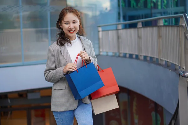 一位快乐 面带微笑的亚洲少女站在购物中心前 手里拿着一个五颜六色的购物袋和一部手机 生活方式技术概念 — 图库照片