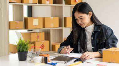 Küçük işletme, KOBİ, Evde çalışan bağımsız girişimci Asyalı kadın, karton kutular, akıllı telefonlar, dizüstü bilgisayarlar, çevrimiçi, pazarlama, ambalaj, ulaşım, KOBİ, e-ticaret kavramı.