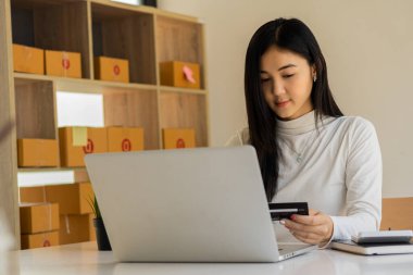 Küçük işletme, KOBİ, Evde çalışan bağımsız girişimci Asyalı kadın, karton kutular, akıllı telefonlar, dizüstü bilgisayarlar, çevrimiçi, pazarlama, ambalaj, ulaşım, KOBİ, e-ticaret kavramı.