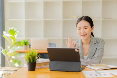 Genç Asyalı bir muhasebeci dizüstü bilgisayarıyla masasında oturuyor ve yatırım sonuçlarını gösteren finansal grafikleri hesaplıyor. Ofiste başarılı bir iş büyüme süreci planlayın.