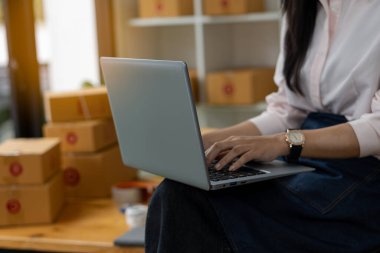 Küçük bir işletme kurun KOBİ girişimcisi veya bağımsız genç Asyalı kadın kutu çevrimiçi pazarlama ve teslimat, KOBİ ev işi kavramı olan bir dizüstü bilgisayar kullanarak.