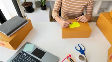 Karton kutular ve sipariş almak için dizüstü bilgisayarla evde çalışan bir kadın KOBİ işine, çevrimiçi alışverişe ve paket teslimatına başlıyor.