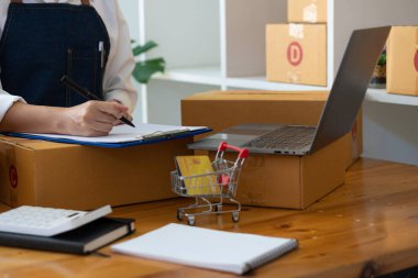 Karton kutular ve sipariş almak için dizüstü bilgisayarla evde çalışan bir kadın KOBİ işine, çevrimiçi alışverişe ve paket teslimatına başlıyor.