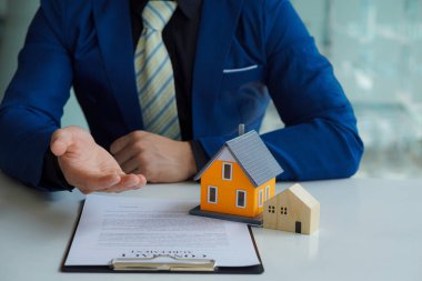 İnsanlar gayrimenkul ve ev alımlarına yatırım yapmak için faiz, vergi ve kâr hesaplıyorlar. Ev düzeni olan emlakçılar müşterilerle ev sigortası hakkında konuşuyorlar..