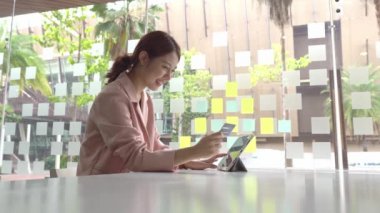 Genç bir kadın elinde bir tabletle internetten kredi kartı alışverişi yapıyor. Bir kadın internet üzerinden bir uygulama üzerinden kredi kartı kullanıyor..