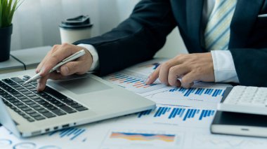 Bir iş adamı ya da muhasebeci masasında iş belgeleri, diyagramlar ve hesap makineleri olan bir dizüstü bilgisayar kullanır. İş adamının elleri ofis finans grafik belgesini analiz ediyor