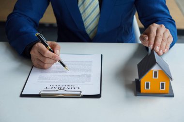 Ev ya da daire almak için sözleşme öneren bir satış temsilcisi. Kağıt döküman sözleşmesi ve tahta masaya yakın kalem ile başarılı iş sözleşmesi için ev