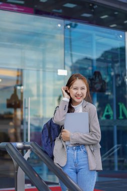 Genç Asyalı öğrenciler bir alışveriş merkezinin önünde tablet ve çanta tutuyorlar. Herkesin içinde.