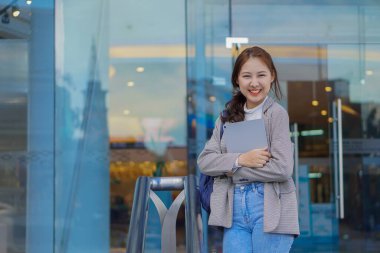 Genç Asyalı öğrenciler bir alışveriş merkezinin önünde tablet ve çanta tutuyorlar. Herkesin içinde.