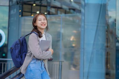 Genç Asyalı öğrenciler bir alışveriş merkezinin önünde tablet ve çanta tutuyorlar. Herkesin içinde.