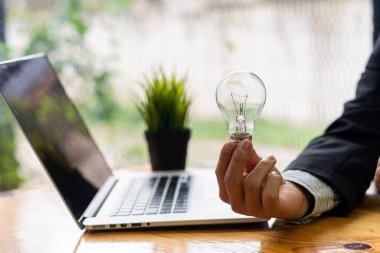 İş adamı elinde bir ampul tutuyor. Belgeler, iş aletleri ve yazı tipleri. Yenilikçi yaratıcı sürdürülebilir iş geliştirme kavramı