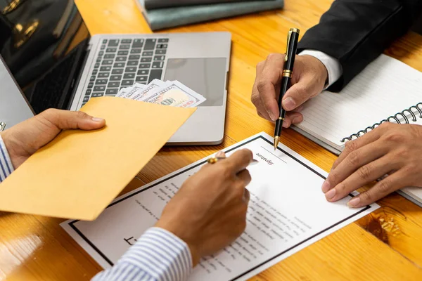 Hands of a businessman who bribed a female colleague who signed a contract in a male office offering a hundred dollar bills. Close-up of a businessman signing a contract Details of signing documents on the table