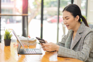 Asyalı kız online alışveriş tableti kullanarak online alışveriş yapıyor. İnternet üzerinden alışveriş yapıyor. Kredi kartı, akıllı telefon, akıllı ödeme, para transferi teknolojisi kullanıyor.