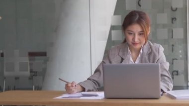Finans muhasebesinde çalışan Asyalı bir kadın dizüstü bilgisayarla iş konsepti tablosunun hesaplama analizinde doküman çiziyor..